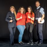 Gloria Wilhelm und Christopher Heuts vom Polizeipräsidium Düsseldorf posieren mit zwei weiblichen Fußballfans aus Albanien und Spanien. Die beiden Frauen tragen jeweils Trikots ihrer Nationalmannschaft und machen eine Daumen nach oben Geste. Alle lächeln.